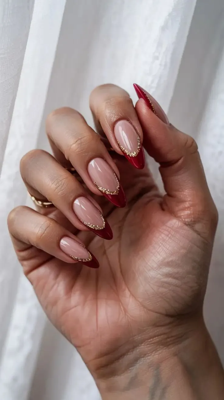 Classy red Christmas French tip nails on almond-shaped nails with a nude base and delicate gold detailing along the tips.